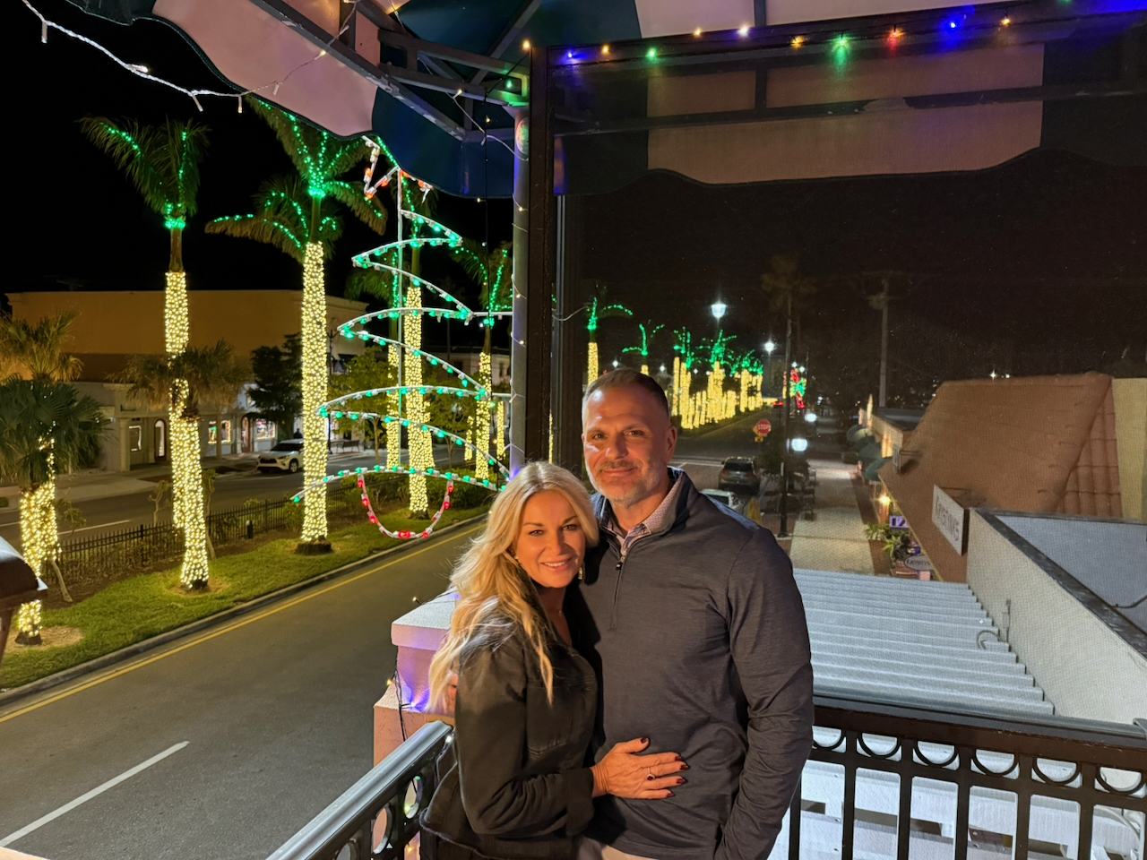 Ruby and DJ together on a balcony at night beneath colorful lights